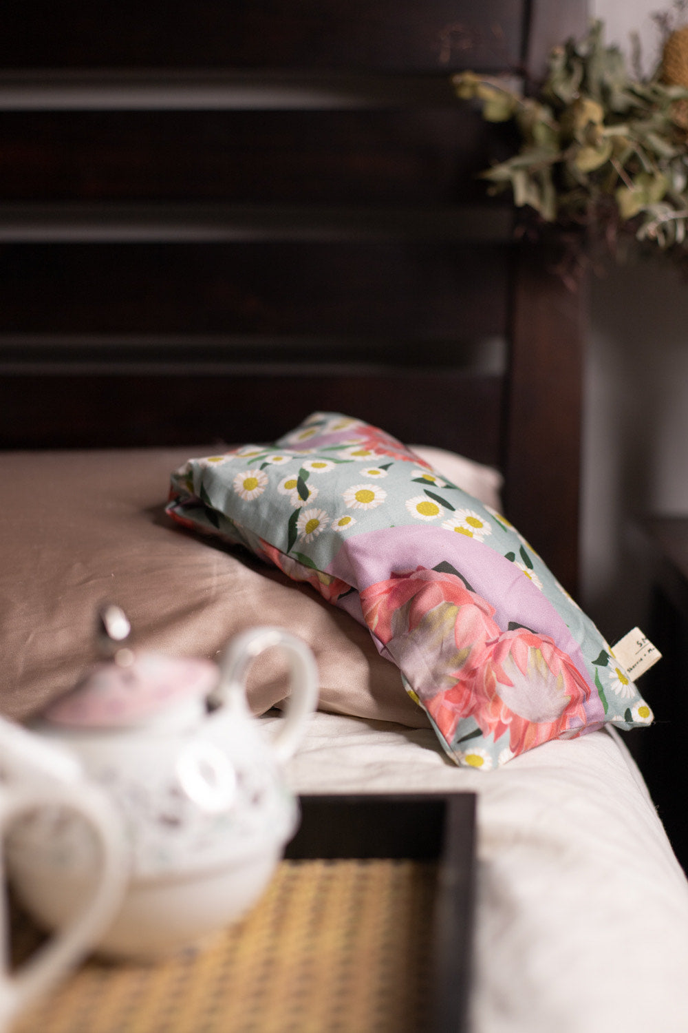 Sherrie Morgan Design relaxing eye pillow with a soft protea and daisy flower print in pink and turquoise, featured on a bed with a relaxing vibe.