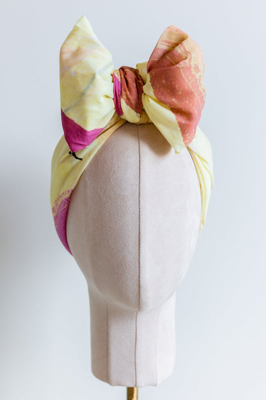 Original Sherrie Morgan design 'Desert Rainbow', comprises a yellow setting with rainbows and shapes in brown, pink and orange, displayed as a headscarf with a large bow, front view