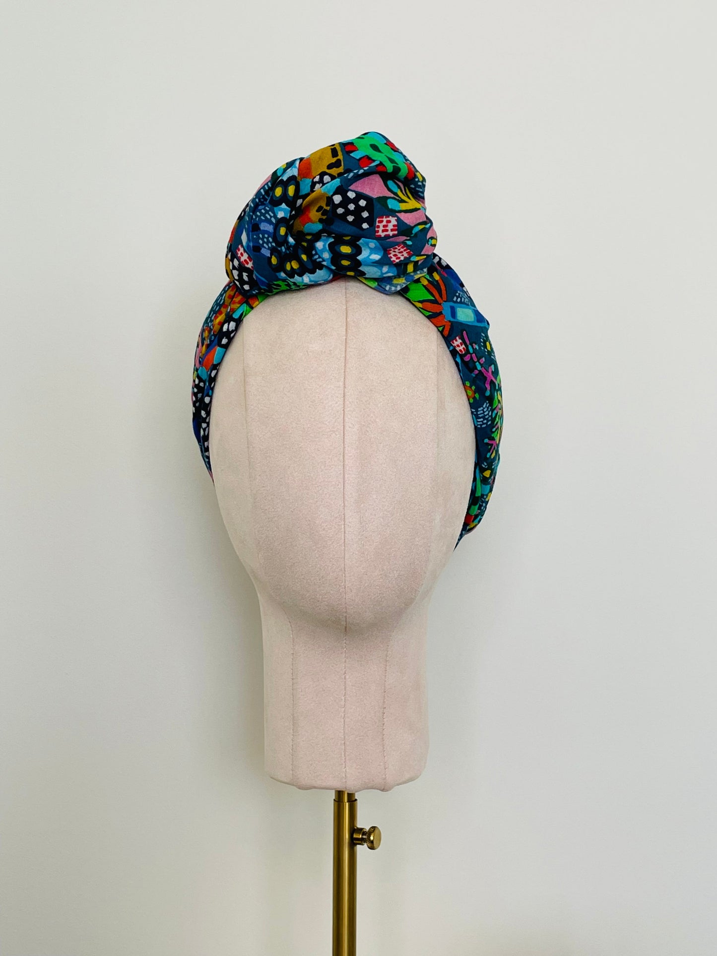 SMD scarf, Miss Moresby abstract multicoloured floral design on a dark grey base, displayed as a headscarf with top knot, front view