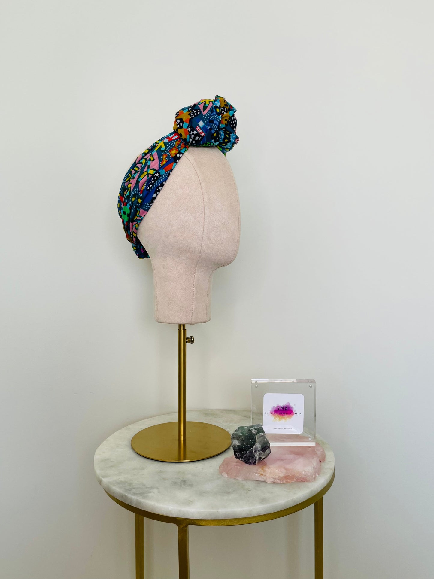 SMD scarf, Miss Moresby abstract multicoloured floral design on a dark grey base, displayed as a headscarf with top knot, side view