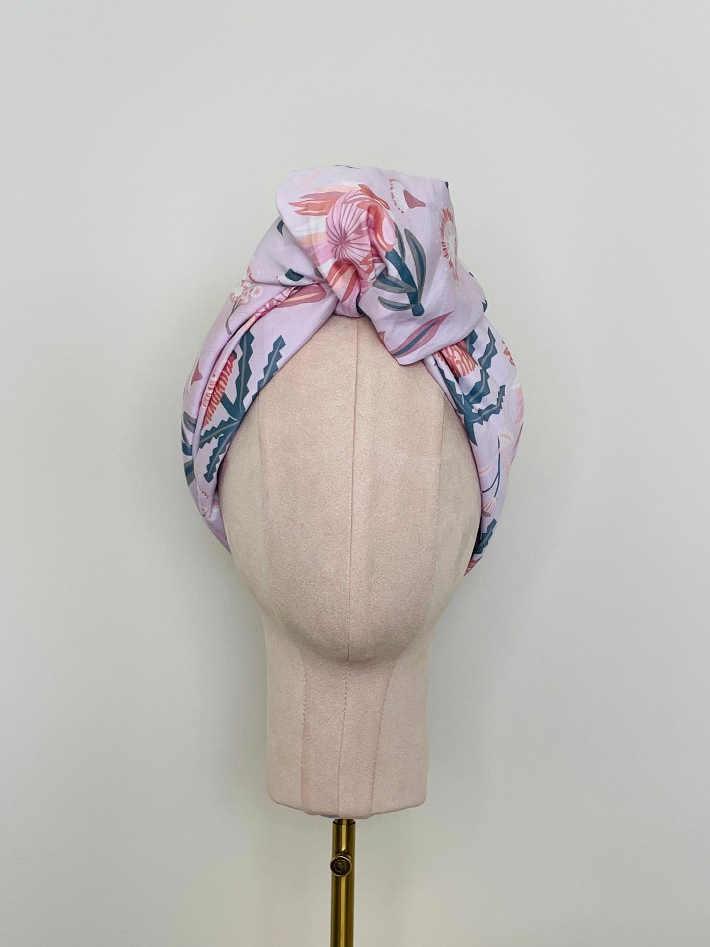 SMD scarf, Christie Williams design of pink proteas and banksia on pink base, displayed as a headscarf with top knot, front view