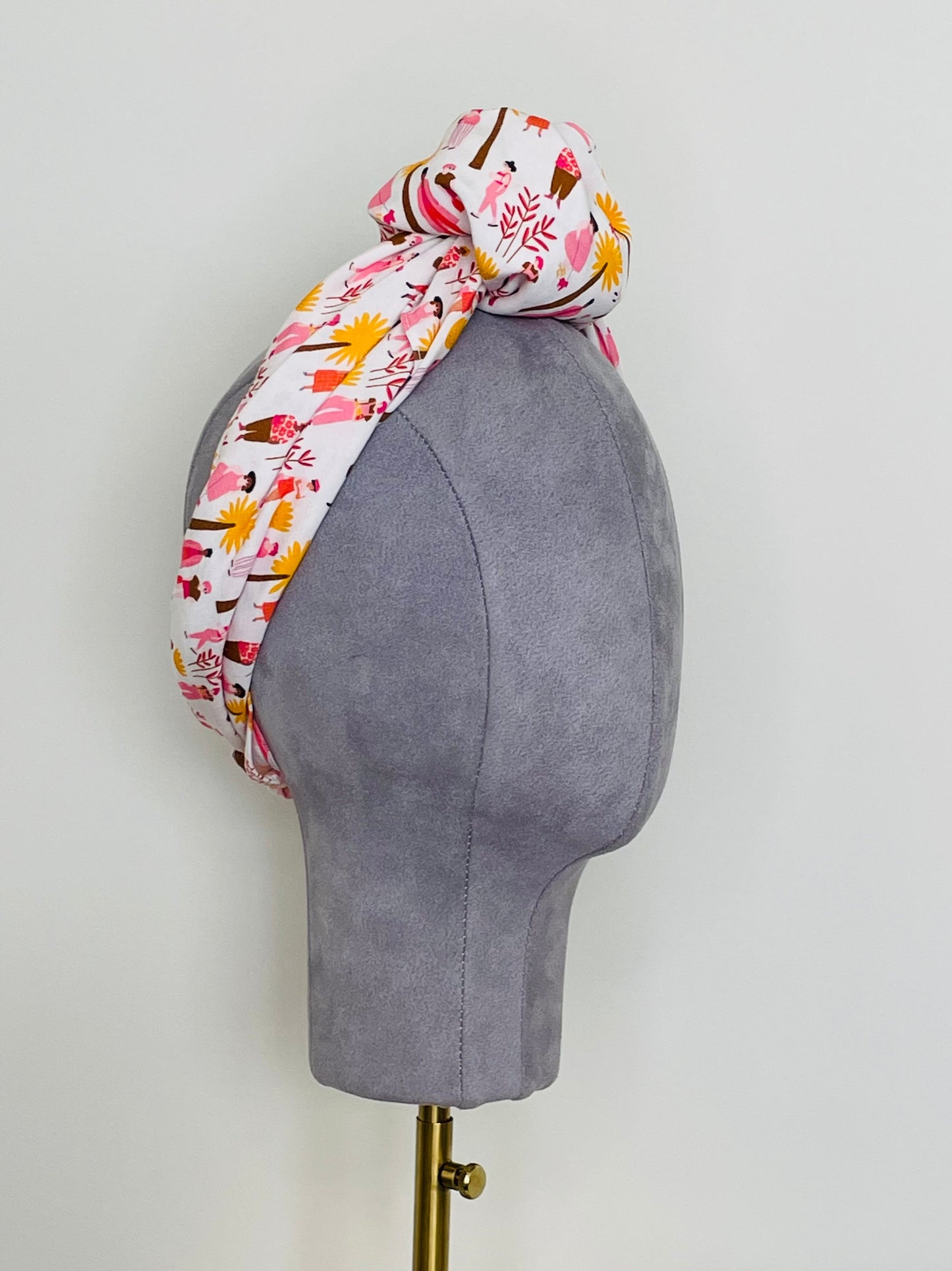 SMD scarf, white base with ladies and dogs walking in pink and yellow, knotted headscarf, side view