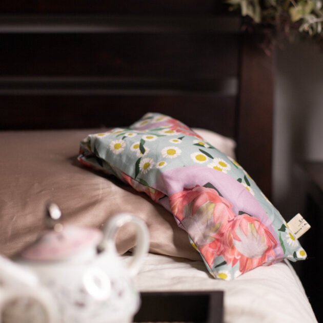 Sherrie Morgan Design relaxing eye pillow with a soft protea and daisy flower print in pink and turquoise, featured on a bed with a relaxing vibe.
