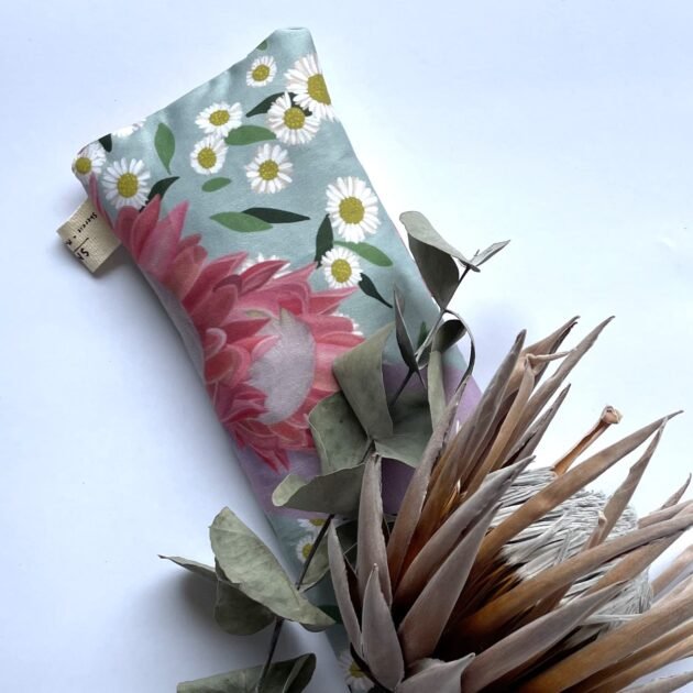 Sherrie Morgan Design relaxing eye pillow with a soft protea and daisy flower print in pink and turquoise, pictured with a dried king protea flower