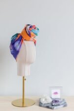 SMD original art 'Party time', vivid orange, blue and green shapes resemble party confetti, displayed as a turban with a large top knot, side view, with with business card