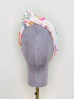 SMD scarf, colourful monstera leaves on a white base, shown as knotted headscarf, front view
