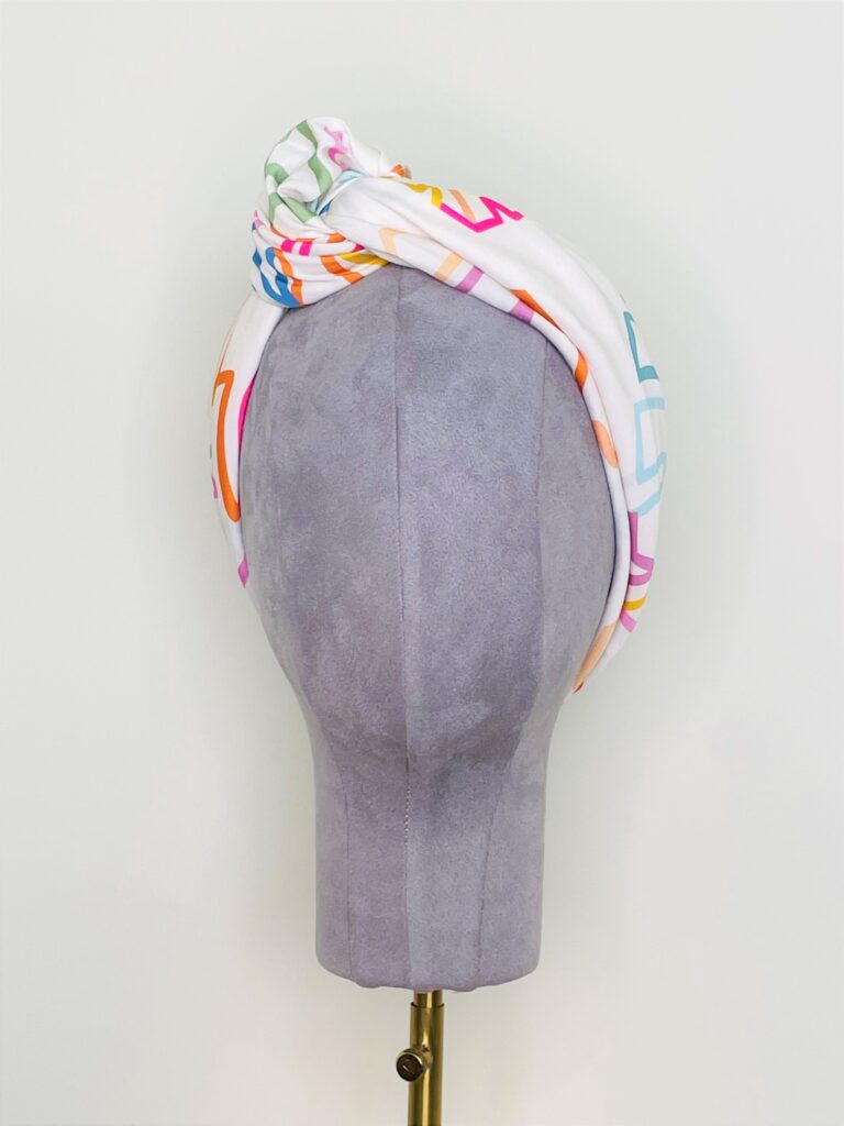 SMD scarf, colourful monstera leaves on a white base, shown as knotted headscarf, front view