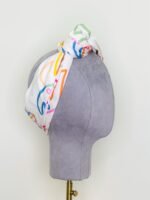 SMD scarf, colourful monstera leaves on a white base, shown as knotted headscarf, side view