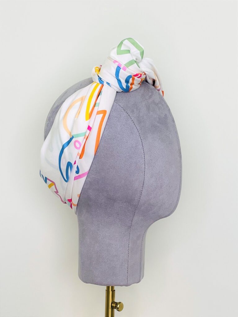 SMD scarf, colourful monstera leaves on a white base, shown as knotted headscarf, side view