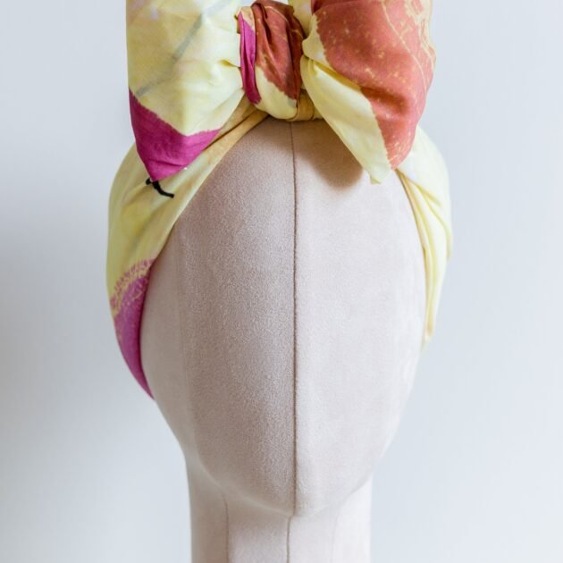 Original Sherrie Morgan design 'Desert Rainbow', comprises a yellow setting with rainbows and shapes in brown, pink and orange, displayed as a headscarf with a large bow, front view