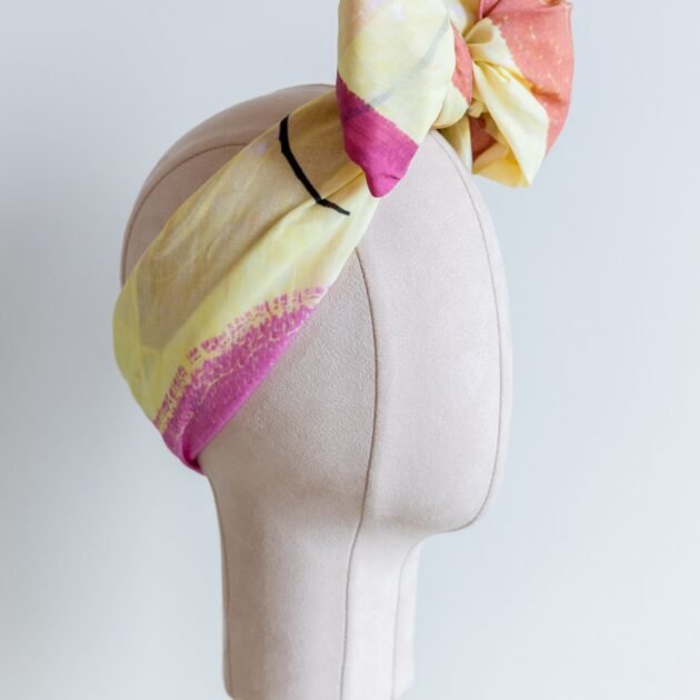 Original Sherrie Morgan design 'Desert Rainbow', comprises a yellow setting with rainbows and shapes in brown, pink and orange, displayed as a headscarf with a large bow, side view