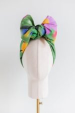 SMD original art 'Flowers for Days', multi coloured flowers in a grassy green field, displayed as headwrap with a large bow, front view.