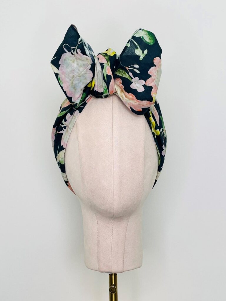 SMD scarf, navy base with a multicoloured floral sea print, shown as a headband with large bow, front view