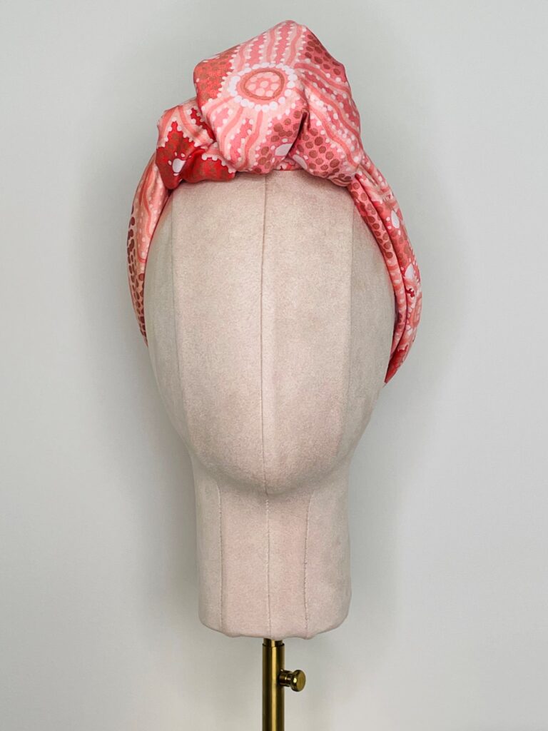 SMD scarf, Emma Stenhouse design in orange, displayed as a headwrap with top knot, front view