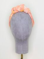 SMD, peachy, birds print on apricot, displayed as knotted crown headscarf, front view.
