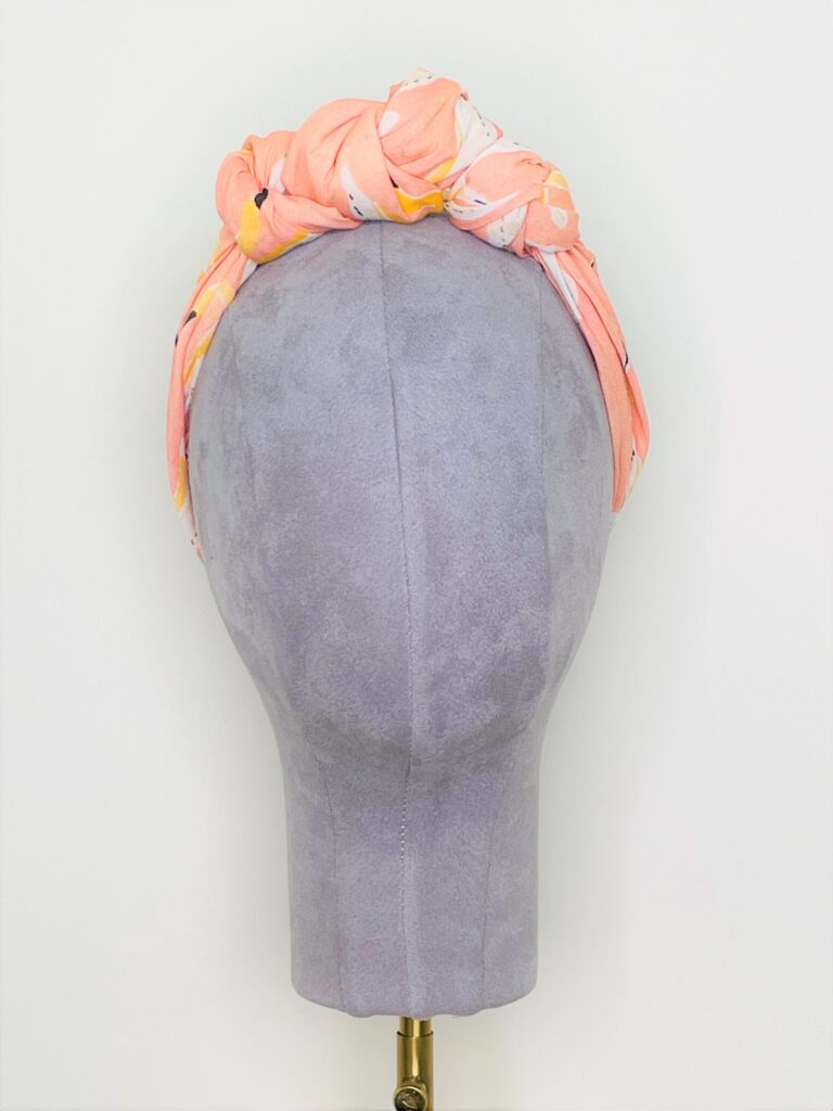 SMD, peachy, birds print on apricot, displayed as knotted crown headscarf, front view.