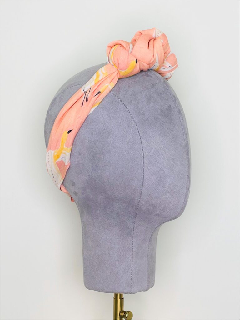 SMD, peachy, birds print on apricot, displayed as knotted crown headscarf, side view.