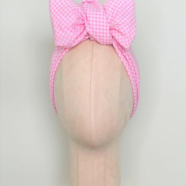 SMD scarf, upcycled pink checkers or gingham fabric, displayed as a headscarf with a bow, front view