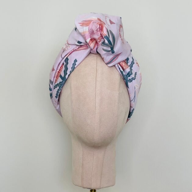 SMD scarf, Christie Williams design of pink proteas and banksia on pink base, displayed as a headscarf with top knot, front view