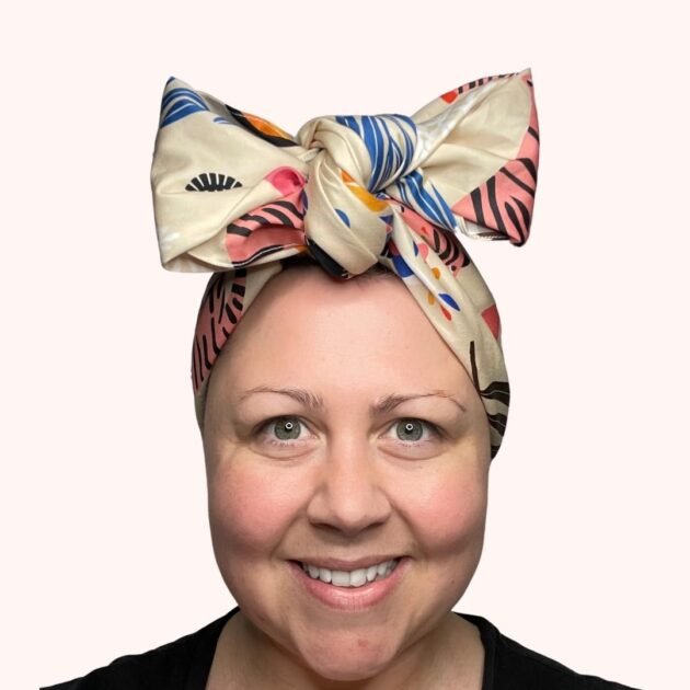 SMD scarf, pink tiger print with ferns and eyes, lisa congdon design shown as a headscarf with large bow