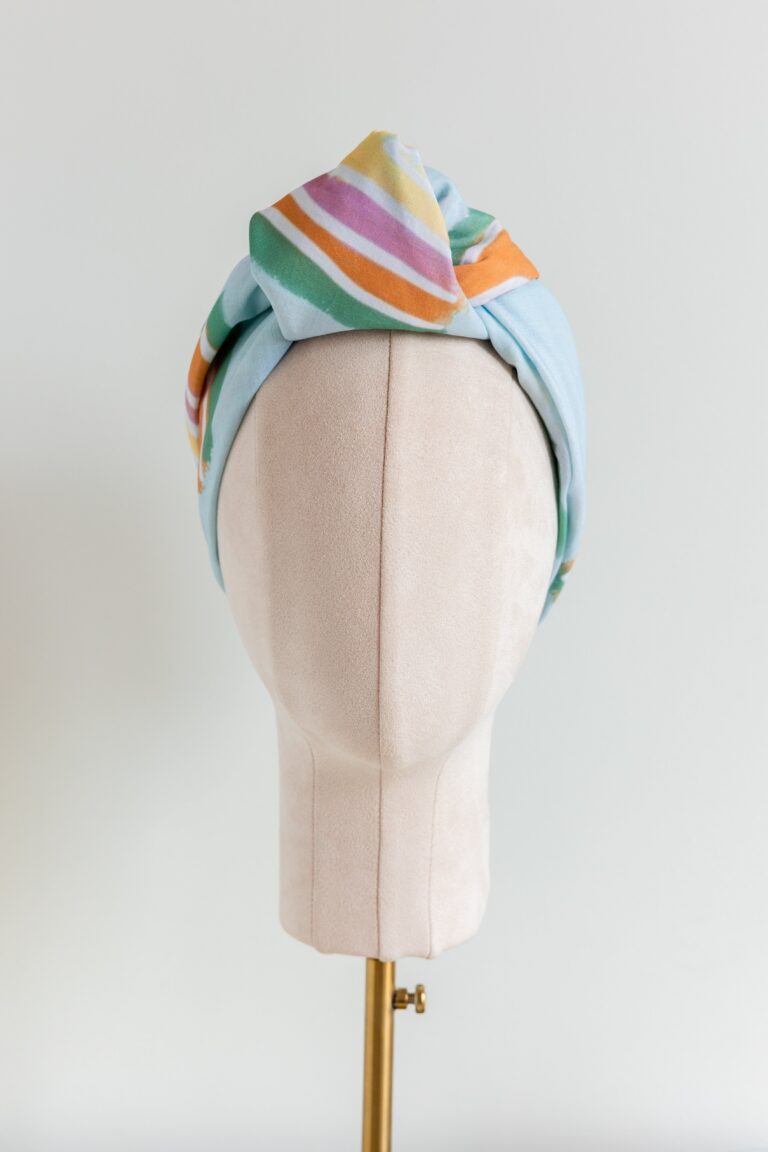 SMD original art 'Rain or Shine', light blue base with rainbows and rain, displayed as a headscarf with flat knot, front view