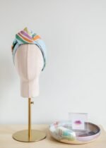 SMD original art 'Rain or Shine', light blue base with rainbows and rain, displayed as a headscarf with flat knot, front view