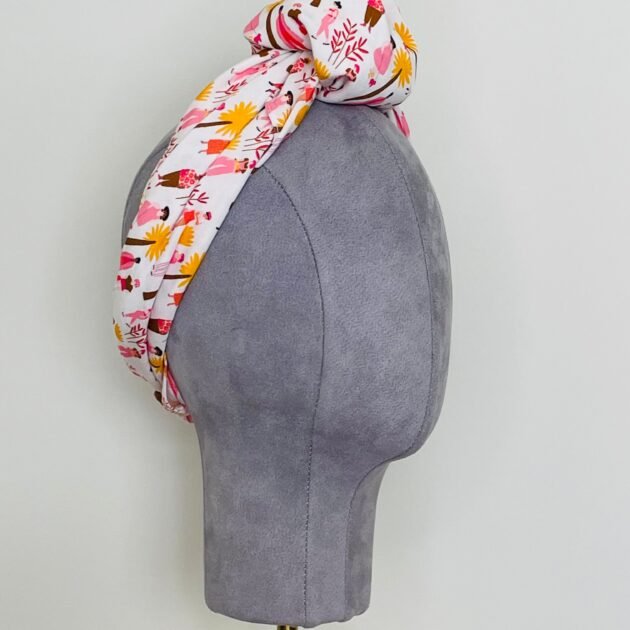 SMD scarf, white base with ladies and dogs walking in pink and yellow, knotted headscarf, side view